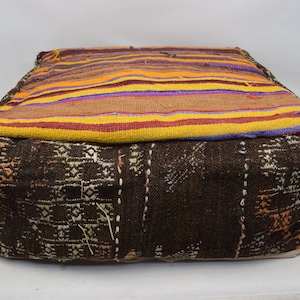 May include: A square, brown and multi-coloured floor cushion with a woven pattern. The cushion is made of fabric and has a striped top.