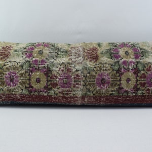May include: A long rectangular cushion with a floral pattern in shades of pink, green, and brown. The cushion has a dark blue border.