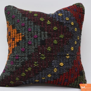 May include: A colorful, handwoven throw pillow with a geometric pattern in shades of red, orange, yellow, green, blue, and purple. The pillow is made of a thick, textured fabric and has a fringe border.