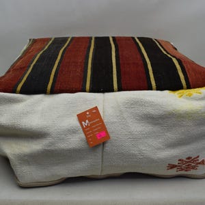 May include: A striped red, black, and cream colored floor cushion with a white cotton cover. The cushion has a tag that says "M - Medium".