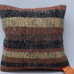 May include: A striped cushion with a brown, black and cream colour scheme. The cushion is made of a textured fabric and has a square shape.
