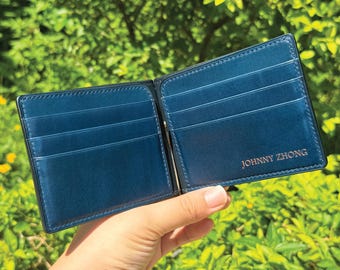 May include: A blue leather wallet with a money clip and multiple card slots. The wallet is open and has the name "JOHNNY ZHONG" embossed on the front.