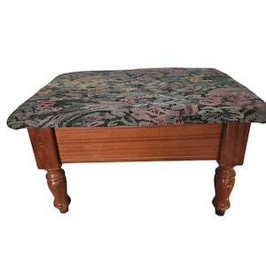 May include: A rectangular footstool with a wooden frame and four turned legs. The top is upholstered in a woven fabric featuring a multi-colored floral pattern in shades of pink, blue, yellow, and green against a dark, textured background.