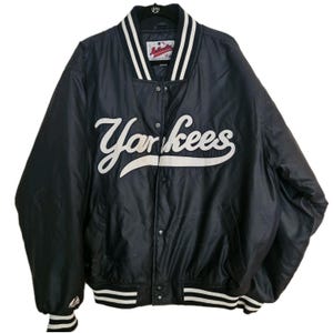 May include: A black Yankees baseball jacket with white lettering and trim. The jacket features the word "Yankees" in large, cursive font across the chest. The collar and cuffs have white stripes.