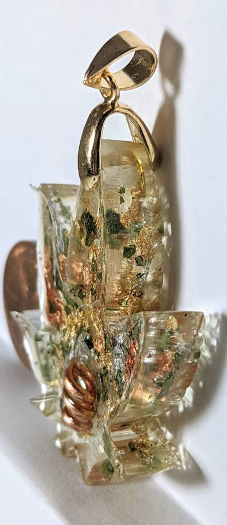 May include: Gold pendant with a clear resin design featuring green, gold, and copper accents. The resin design is reminiscent of a flower or a leaf.