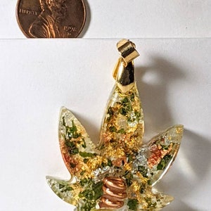 May include: Gold-tone pendant featuring a clear resin leaf with embedded green and gold flakes, copper wire, and a gold-tone bail.