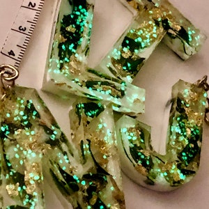 May include: Three resin letter charms with a green and gold marbled design. The letters are K, U, and N.