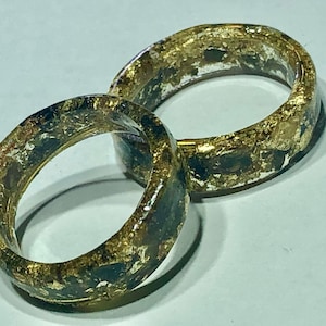 May include: Two gold and black resin rings with gold leaf accents. The rings are interlocked and have a glossy finish.