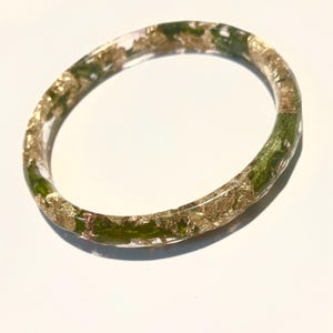 May include: A clear resin bangle bracelet with gold leaf and green accents.