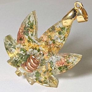 May include: A gold-tone pendant in the shape of a marijuana leaf with green, gold, and silver glitter embedded in clear resin. The pendant has a copper-tone bail.
