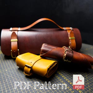 Op de afbeelding: Drie leren rol-etuis in bruin, beige en geel. De etuis zijn van leer en hebben een band met een gesp. De etuis liggen op een zwart-wit geblokt oppervlak. PDF-patroon.