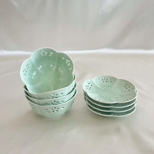 May include: A set of six light green ceramic bowls and saucers. The bowls are stacked, and the saucers are in a separate stack. Each piece has a scalloped edge and a floral cut-out design.