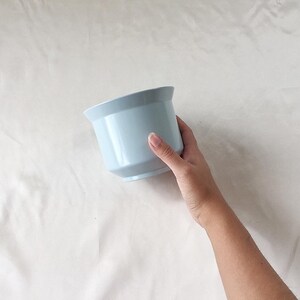 Peut inclure: Un pot de fleurs en c&eacute;ramique bleu clair. Le pot est rond avec un bord l&eacute;g&egrave;rement &eacute;vas&eacute;.