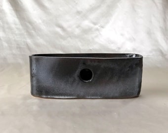 May include: A black ceramic planter with a single drainage hole. The planter has a rectangular shape with rounded edges.