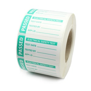 May include: A roll of white labels with green detailing. Each label is marked "ELECTRICAL SAFETY TEST" and has spaces for "TEST DATE", "TESTED BY", and "APP I.D.". The word "PASSED" is printed vertically on the side of each label.