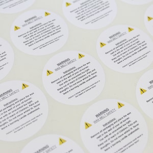 May include: Close-up of multiple white round warning labels with a yellow triangle and exclamation point. The labels contain the text "WARNING WAX MELT SAFETY" and instructions for using wax melts safely.
