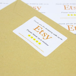 May include: A white sticker with the text "Thank you for shopping with us on Etsy. Please leave us a review." and five yellow stars. The sticker is on a brown paper envelope.