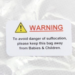 May include: A white warning label with a yellow triangle containing an exclamation point. The text reads "WARNING To avoid danger of suffocation, please keep this bag away from Babies & Children."