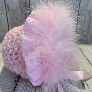 May include: A pink crocheted baby hat with a fluffy pink feather trim and a pink satin ribbon.