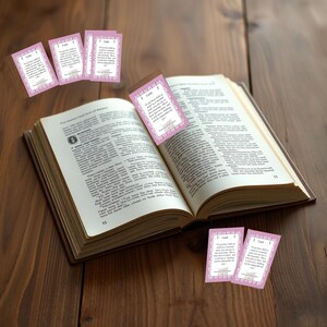 May include: An open book with a brown cover and pages. Several pink bookmarks with the word "Faith" and a quote are placed in and around the book. The bookmarks have a decorative border and are scattered on a wooden surface.