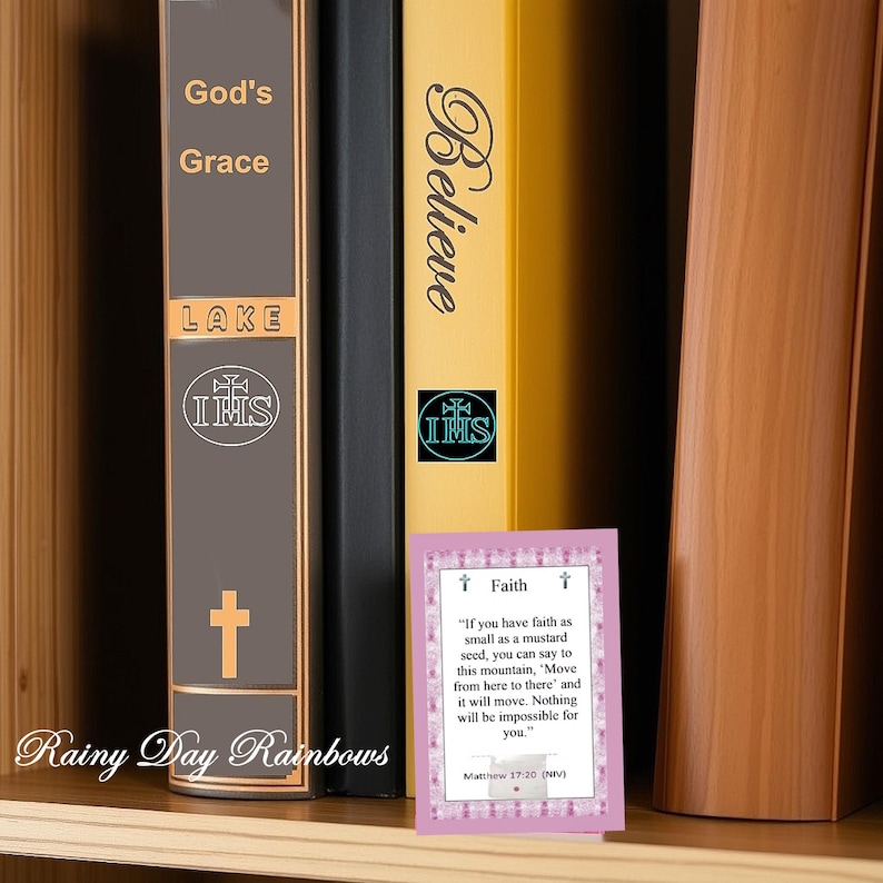 May include: A wooden bookshelf displaying three books and a small card. The books are titled "God's Grace", "Believe", and "LAKE". The card features a quote about faith from Matthew 17:20. The text "Rainy Day Rainbows" is visible.