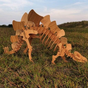 May include: A wooden model of a Stegosaurus dinosaur skeleton, standing in a grassy field. The model is made of plywood and has a detailed design.