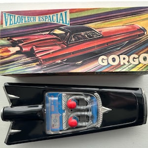 May include: A black toy spaceship with red details and a clear plastic window showing the interior. The box shows a red and black futuristic car with the text "VELOFLECH ESPACIAL GORGO" on it.