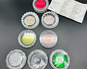 May include: A set of eight round, clear plastic containers with colored filters inside. The filters are red, yellow, green, pink, light brown, and gray. The containers have a starburst design on the outside.