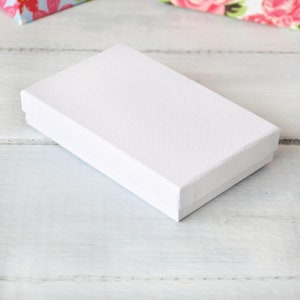 May include: A white rectangular box with a textured surface. The box is empty and sitting on a white wooden surface.