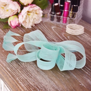 May include: A light blue fabric bow with a frayed edge. The bow is made of a soft, delicate material and has a flowing, elegant shape.