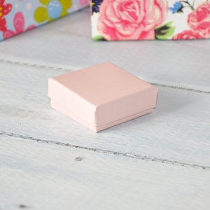 May include: A small, pale pink, square-shaped box with a smooth surface.