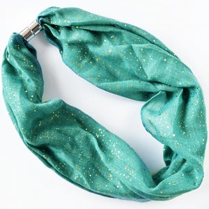 May include: A teal infinity scarf with gold flecks and a silver magnetic clasp. The scarf is made of a soft, flowing fabric and is designed to be worn around the neck. This accessory adds a touch of elegance to any outfit.