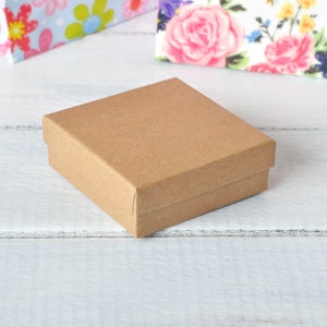 May include: A small, brown cardboard box with a lid. The box is sitting on a white wooden surface.