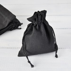 May include: A black drawstring pouch made of fabric. The pouch is closed and has a gathered top.