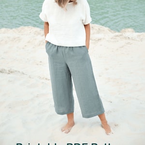 May include: A person wearing a white top, and teal culottes, and a straw hat stands on a sandy beach. The text "Split Skirt / Culottes" and "Printable PDF Pattern" are visible in the image. The culottes are a wide-leg style.