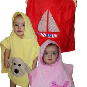 Op de afbeelding: Drie badcapes met capuchon voor kinderen, één rood met een zeilbootontwerp, één geel met een hondenontwerp en één roze met een kroontje.