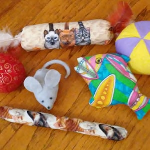 May include: A set of cat toys including a plush fish, a mouse, a ball, a feather wand, and two catnip toys. The toys are made of fabric and have various colors and patterns.