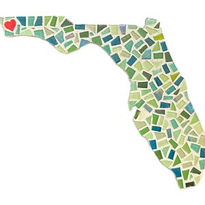 May include: Mosaic art piece in the shape of Florida, featuring a mosaic design of green, blue, and white tiles. A red heart is placed in the upper left corner. The artwork is set against a white background.