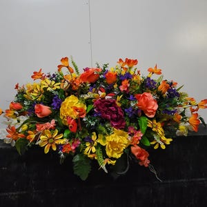 May include: A colorful floral arrangement with orange, yellow, pink, and purple flowers. The arrangement is on a black surface.