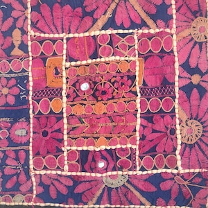 Puede incluir: Textil bordado cuadrado con borde negro. El diseño presenta un patchwork de patrones florales y geométricos azules y rosas, con detalles en naranja y blanco. Se incorporan pequeños espejos en el diseño.