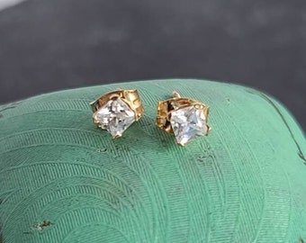 May include: A pair of gold stud earrings with clear square-shaped gemstones.