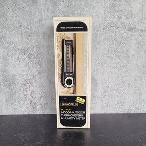 Puede incluir: Un termómetro interior-exterior blanco y negro y un higrómetro con una caja blanca que dice "Sutton Springfield Plus Metric Indoor-Outdoor Thermometers & Humidity Meter".