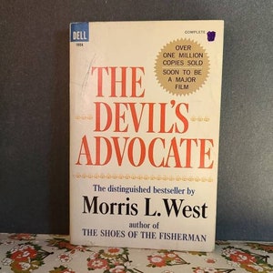 May include: A Dell paperback book titled "The Devil's Advocate" by Morris L. West, author of "The Shoes of the Fisherman". The book cover is white with red and black text. A sticker on the cover reads "Complete, Over One Million Copies Sold, Soon to be a Major Film."