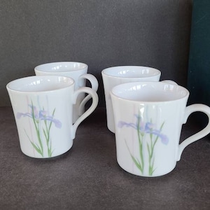 Puede incluir: Juego de cuatro tazas de cerámica blanca con un diseño floral que presenta iris púrpuras y hojas verdes. Las tazas tienen un diseño simple y elegante y son perfectas para el uso diario.