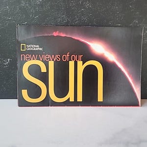 May include: A National Geographic magazine cover with the title "new views of our SUN" in yellow letters. The background is dark with a red and orange illustration of the sun. The National Geographic logo is in the upper left corner.