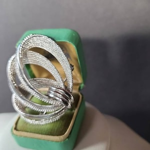 May include: A silver ring with a swirling, multi-layered design. The ring is in a green velvet box.