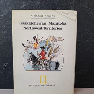 May include: A vintage National Geographic book titled "Close-Up: Canada" featuring illustrations of a mounted figure, birds, and wheat. The cover text reads "Saskatchewan Manitoba Northwest Territories."