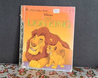 Puede incluir: Un pequeño libro dorado con la película de Disney El Rey León. La portada muestra a Simba y Mufasa, ambos con pelaje naranja, mirándose. El libro es un cuento clásico para niños.