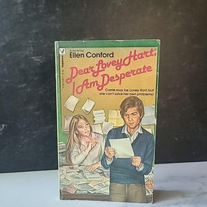 May include: A vintage paperback book titled "Dear Lovey Hart, I Am Desperate" by Ellen Conford. The cover features a green border and an illustration of a man and woman surrounded by papers. The book is a novel.