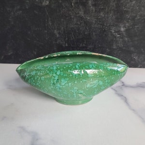 May include: A green ceramic bowl with a speckled glaze. The bowl is oval shaped and has a slight lip around the edge.